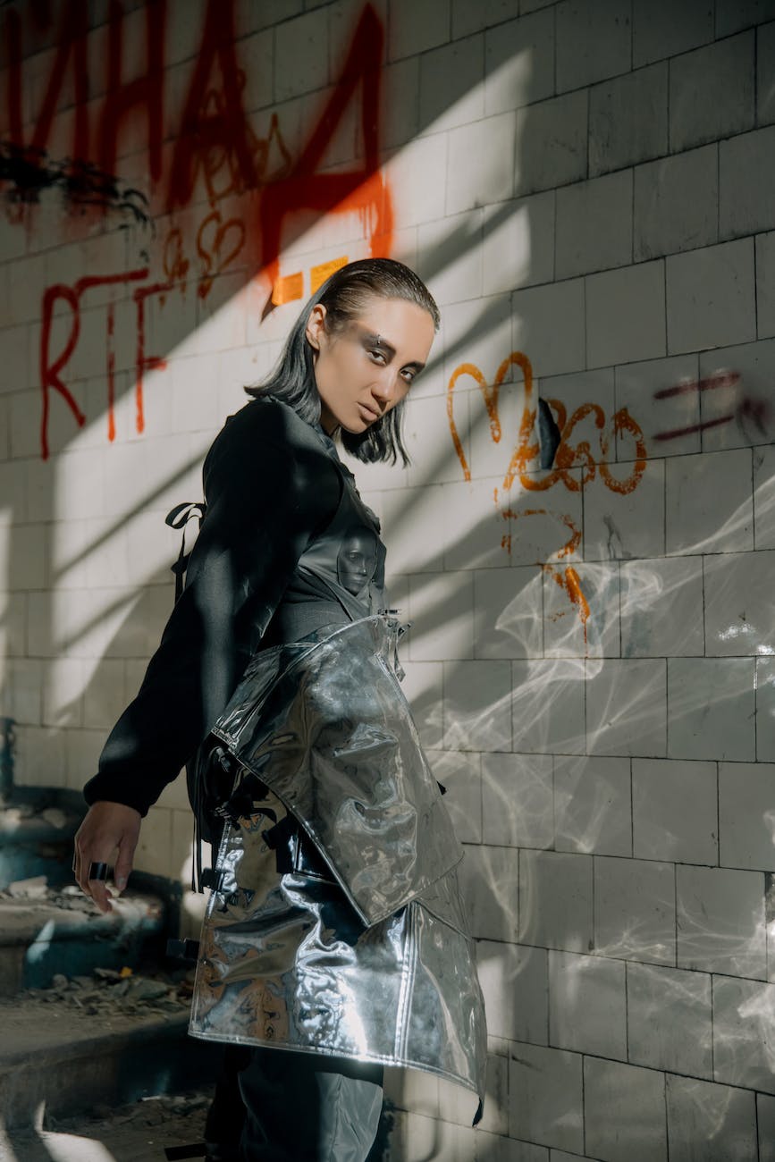 woman in black leather jacket and black pants standing beside white wall